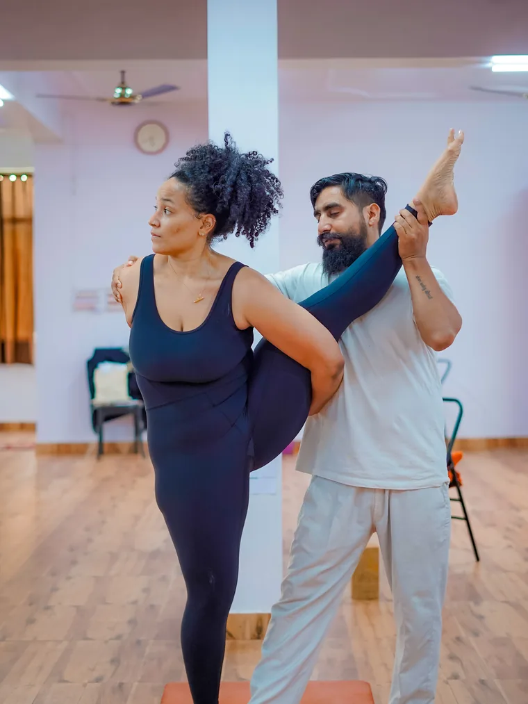 Yogi Manoj adjusting a student in Akarna Dhanurasana, the archer pose