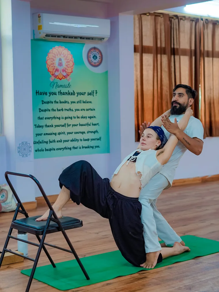 Yogi Manoj supporting a student through a chair-assisted backbend